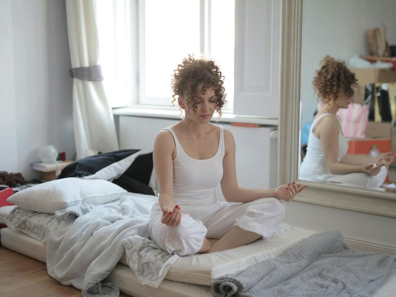 Woman sitting in a peaceful meditation pose near a window.